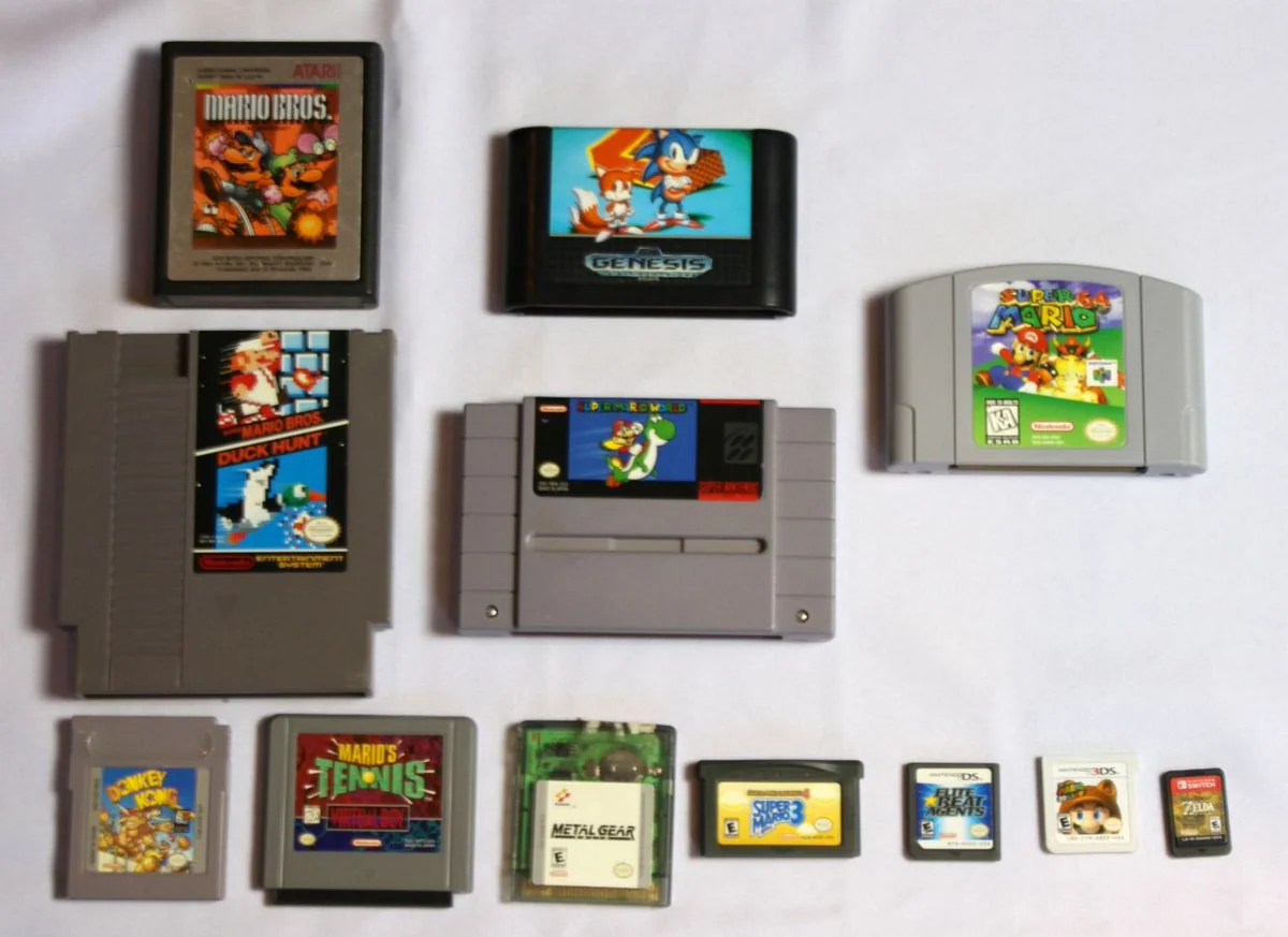 A collection of various retro video game cartridges from consoles like NES, SNES, Genesis, N64, Game Boy, and DS, laid out on a white background. The labels show colorful game art and titles.
