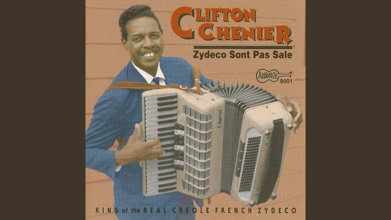 A smiling man in a blue suit holds an accordion on the album cover for "Zydeco Sont Pas Sale" by Clifton Chenier. The text includes the artist’s name and the album title, with a tagline calling him the king of Creole French zydeco.