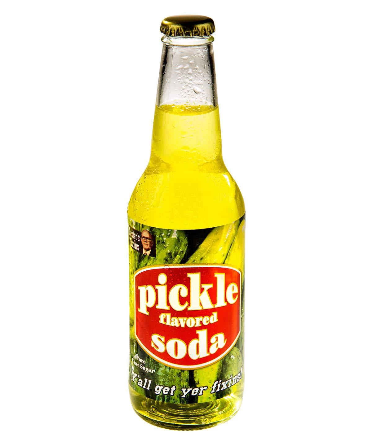 A glass bottle of pickle flavored soda with a yellow-green liquid inside. The label reads "pickle flavored soda" in bold red and white letters, featuring images of pickles and the phrase "Y'all get yer fixins!" at the bottom.
