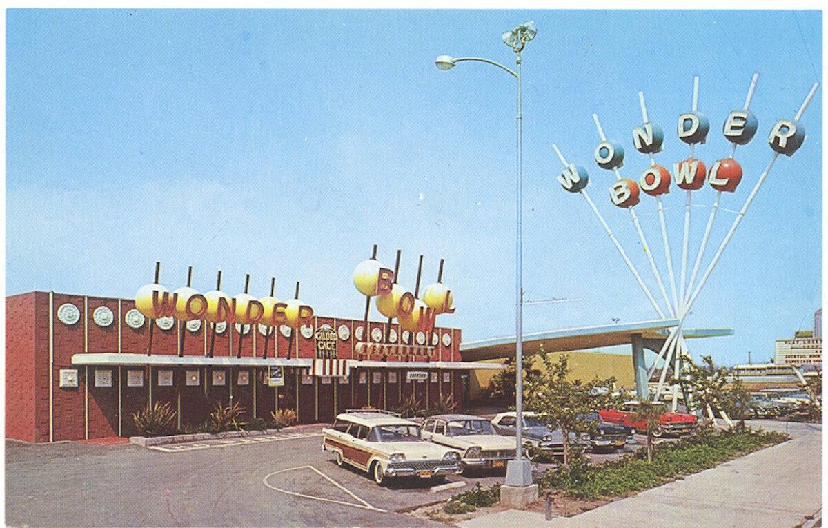 A vintage bowling alley called Wonder Bowl, with large colorful sign letters on tall poles and classic cars parked in front; building has a mid-century design with decorative clocks.