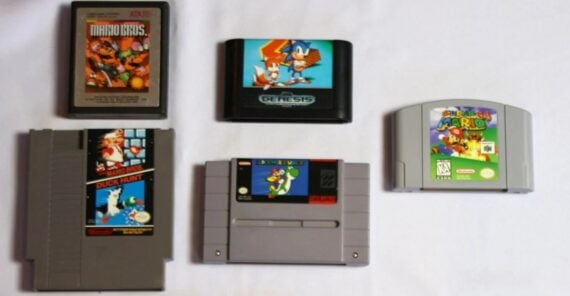 Five classic video game cartridges from different consoles are arranged on a white surface, including titles for Atari, NES, Sega Genesis, SNES, and Nintendo 64.