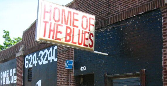 A brick building with a large sign reading "HOME OF THE BLUES" in red letters, a street number "423," and a partial phone number painted on the wall.