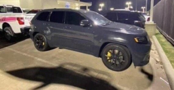 A dark gray SUV appears to be floating above the ground in a parking lot at night, due to the shadow aligning perfectly with its wheels. Other vehicles and streetlights are visible in the background.