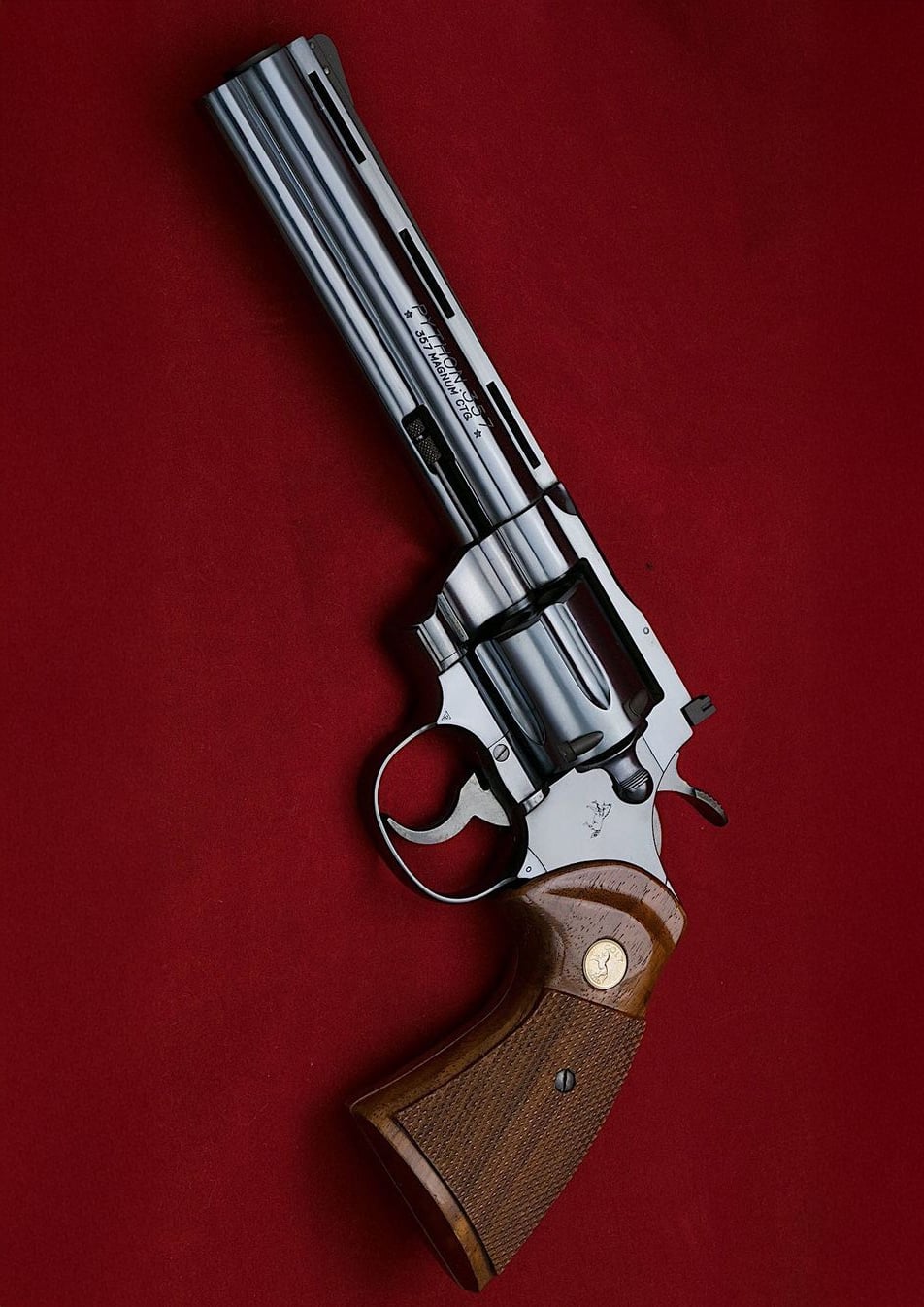 A polished silver revolver with a long barrel and wooden grip is displayed on a deep red background.