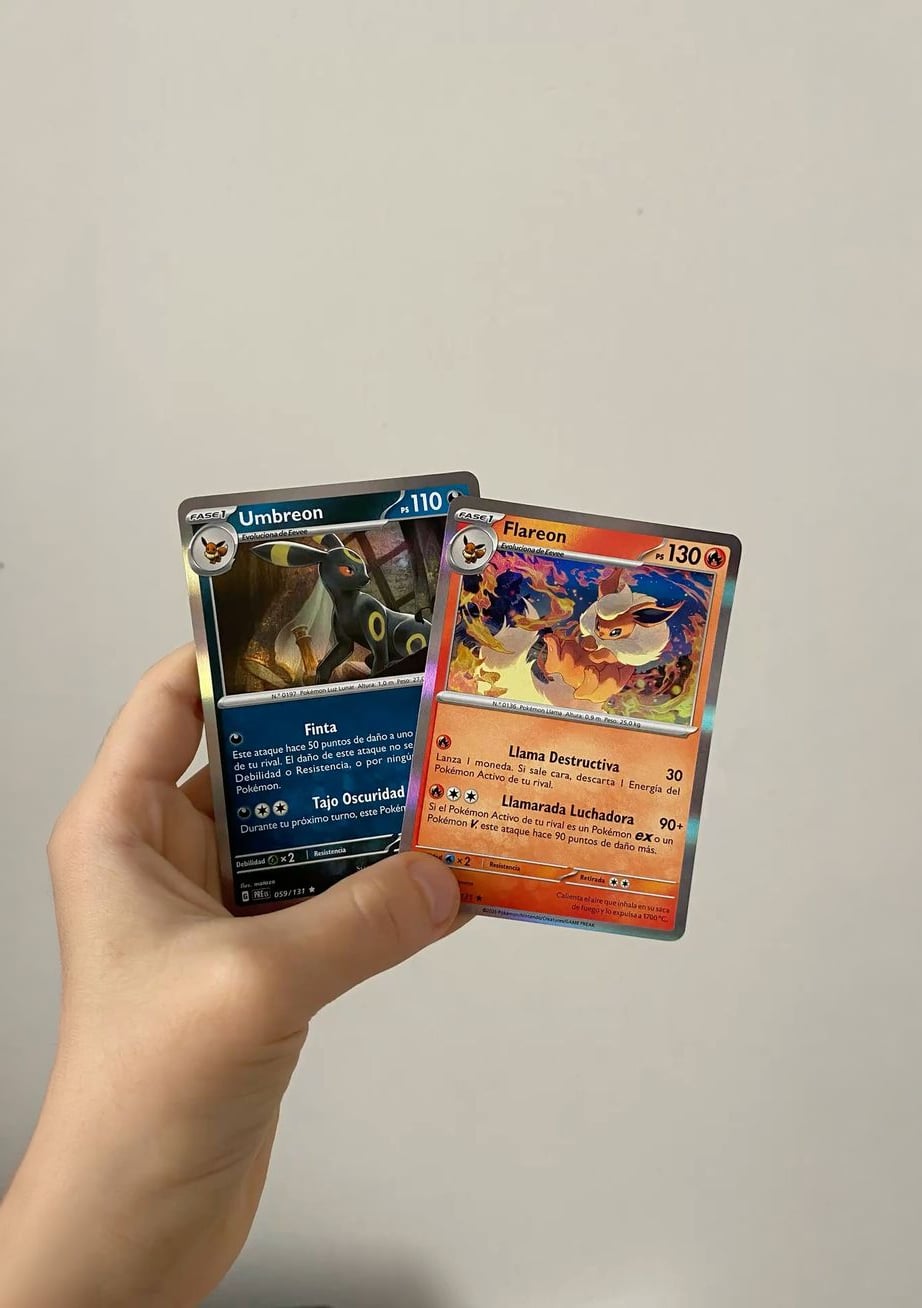 A hand holding two Pokémon cards: Umbreon on the left, with a blue background, and Flareon on the right, with a red background, against a plain light-colored wall.