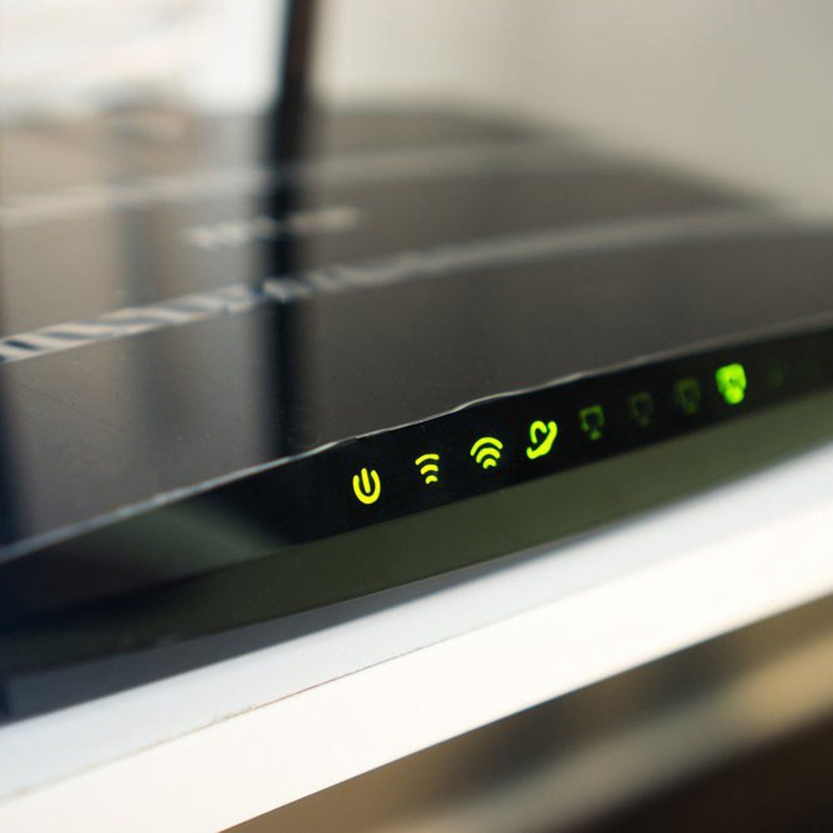 Close-up of a black wireless router showing several green status indicator lights, including power, Wi-Fi, internet, and connection symbols, on a white surface.