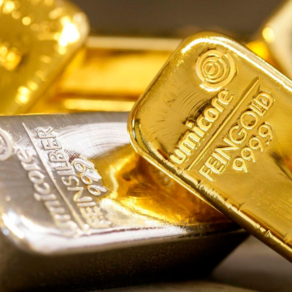 Close-up of stacked gold and silver bars, with "Feingold 999.9" engraved on the gold bar and "Feinsilber 999" on the silver bar. The bars reflect light, highlighting their shiny surfaces and detailed engravings.