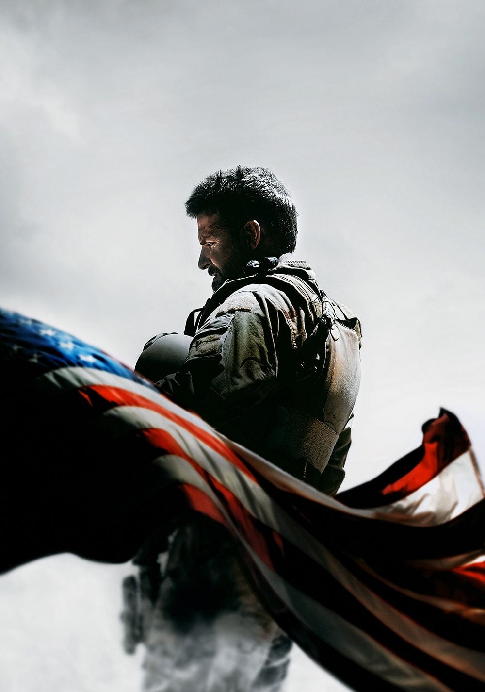 A soldier in combat gear stands with his helmet under his arm, looking down thoughtfully. An American flag waves prominently in the foreground against a cloudy sky.
