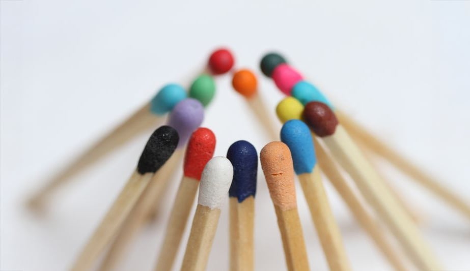 A group of wooden matchsticks with match heads in various bright colors are arranged in a semicircle, standing upright on a white background.