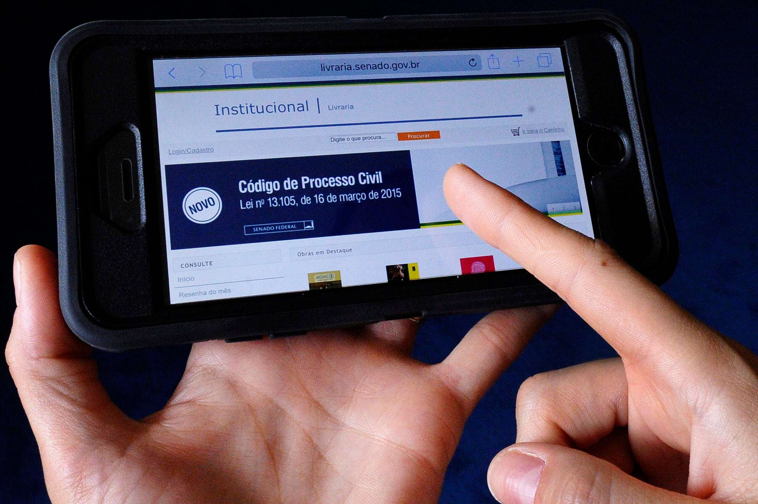 A person holds a smartphone and uses their finger to browse a website about the Código de Processo Civil, highlighting the law passed on March 16, 2015, displayed on the device screen.