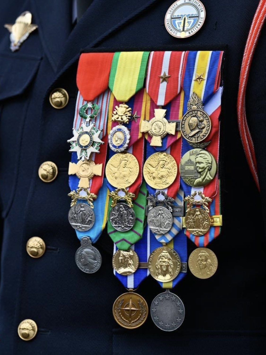 A close-up of a person in a dark military uniform displaying numerous colorful ribbons and medals on their chest, showcasing various awards, honors, and insignia.