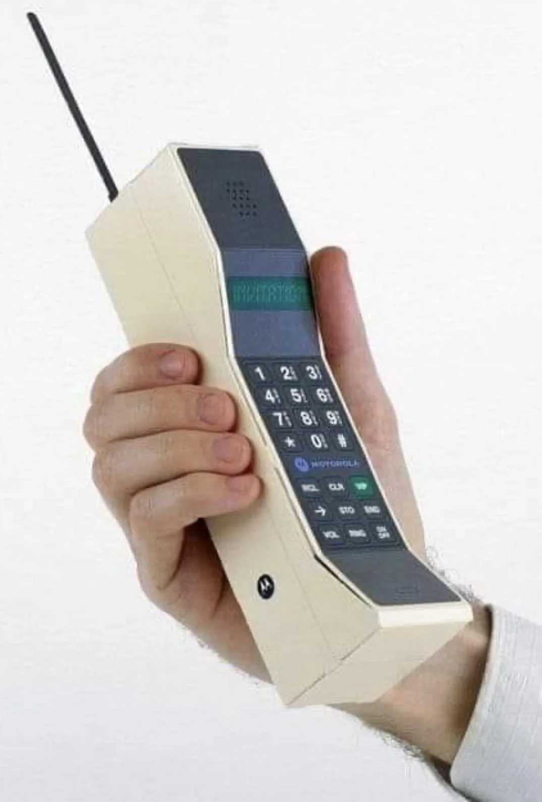 A hand holding a large, vintage Motorola mobile phone with a physical keypad, an antenna, and a small display screen. The phone has a beige and black color scheme.