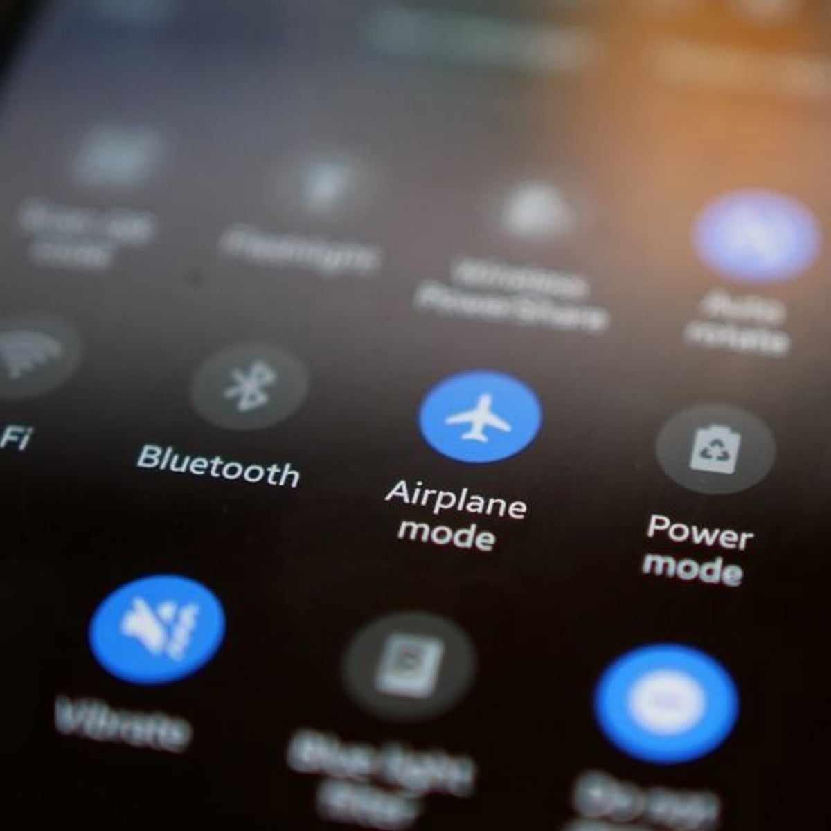 A close-up of a smartphone screen showing quick settings icons, including WiFi, Bluetooth, Airplane mode, and Power mode. The Airplane mode icon is highlighted in blue.