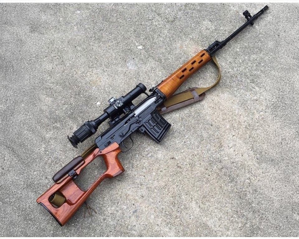 A Dragunov sniper rifle with a wooden stock, scope attached, and a sling, resting on a concrete surface.