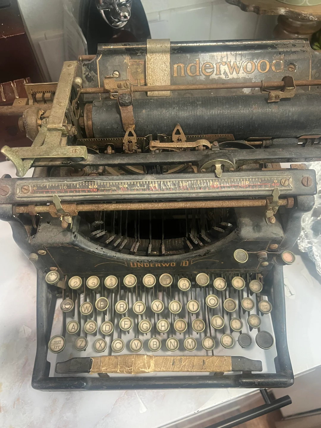 An old, worn Underwood typewriter with round, raised keys and visible metal mechanisms, showing signs of rust and age on its black and gold frame.