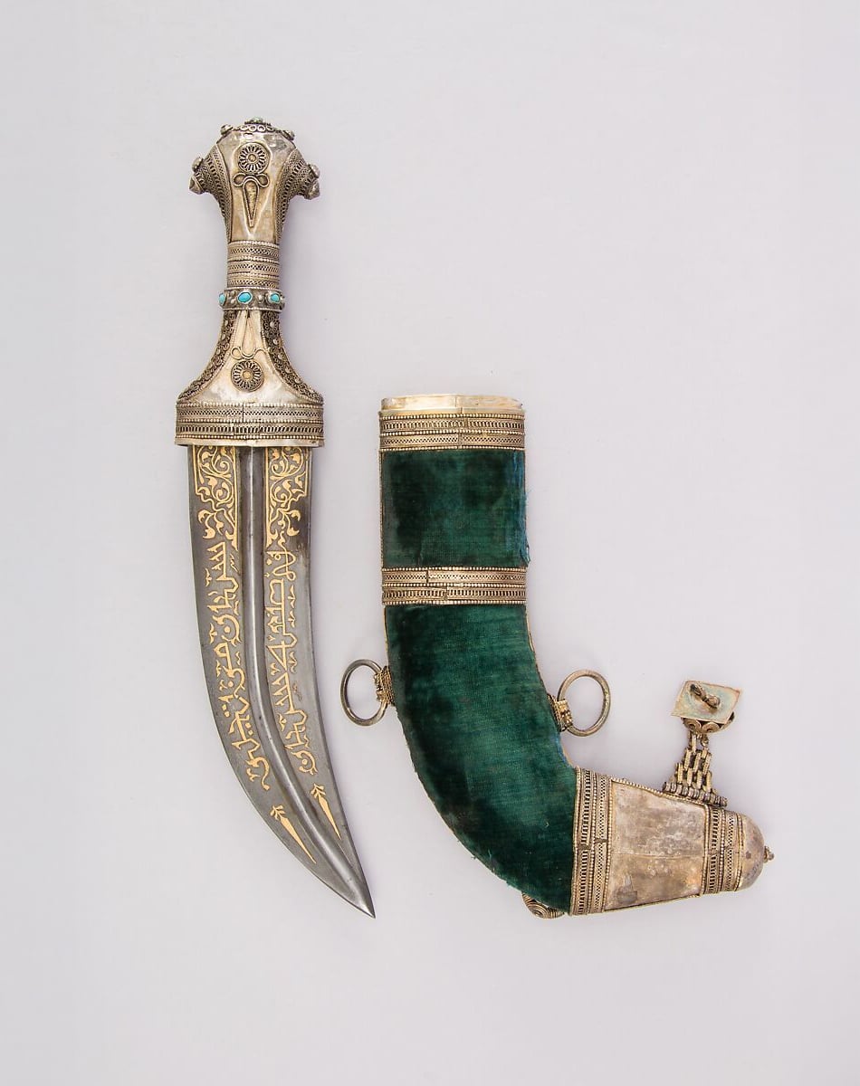 A decorative dagger with an ornate silver and gold hilt and blade featuring intricate designs, placed next to a green velvet-curved sheath adorned with silver fittings and detailed metalwork.