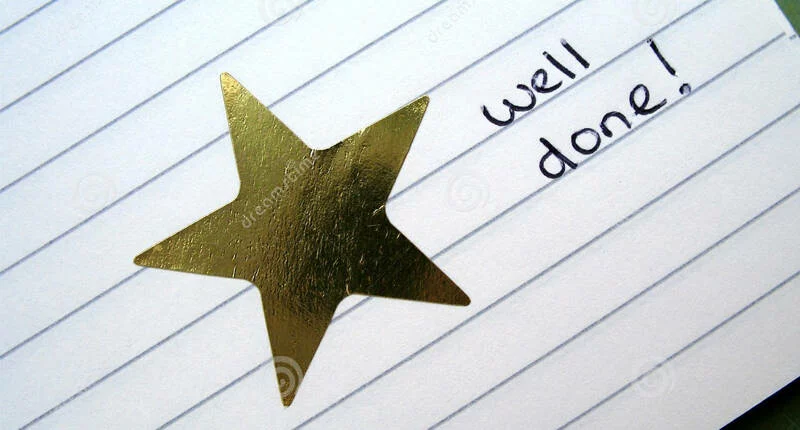 A gold star sticker is placed on a lined piece of paper with the handwritten words "well done!" written next to it in black ink.