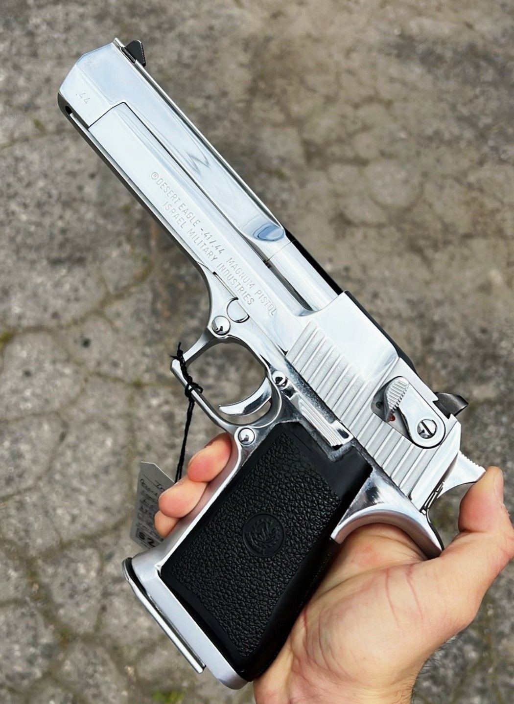 A person holding a shiny silver Desert Eagle pistol with a black grip, outdoors on a paved stone surface.