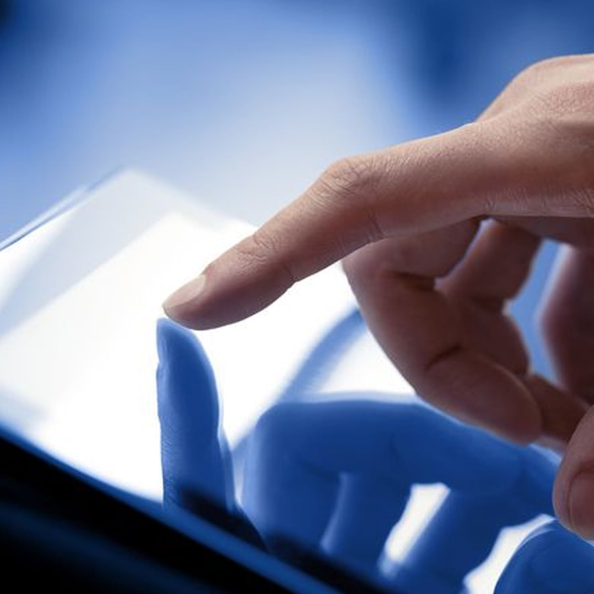 A close-up of a person's hand using their index finger to touch the screen of a tablet device, with a blue background and a clear reflection visible on the screen.