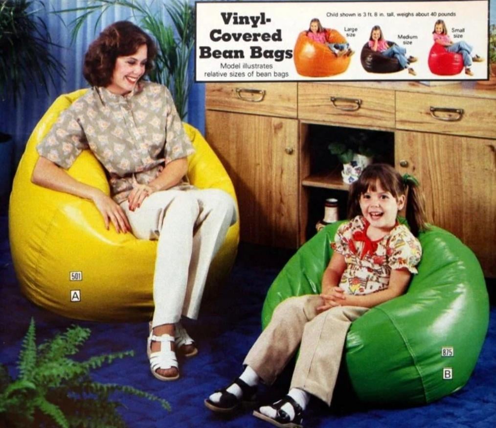 A woman sits on a large yellow bean bag chair and a young girl sits on a green bean bag chair. Behind them is a wooden cabinet, blue wall, and plants. An inset shows various vinyl-covered bean bag sizes and colors.