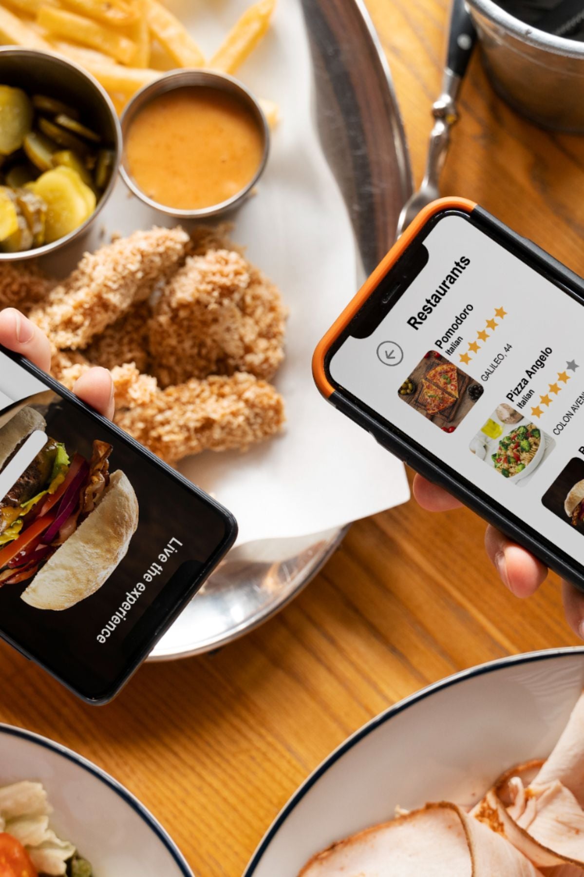 Two people sit at a table with fried chicken, fries, and sauce, each holding a phone—one displays a burger photo, the other shows a restaurant delivery app with food options.