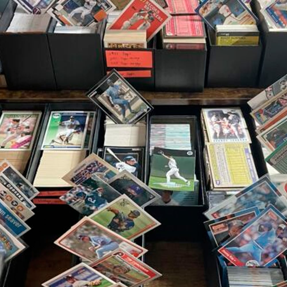 Boxes filled with assorted sports trading cards, many featuring baseball players, are spread out and overlapping on a table in a casual, disorganized arrangement.