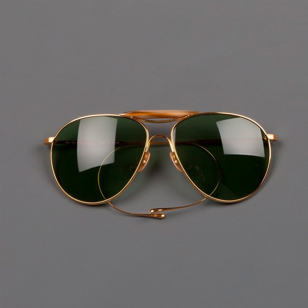 A pair of gold-framed aviator sunglasses with dark green lenses is displayed on a plain gray background.