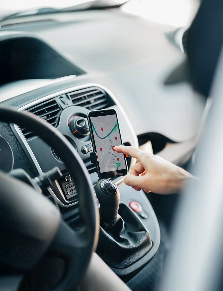 A person sitting in a car uses their finger to navigate a map on a smartphone mounted on the dashboard near the gearshift.