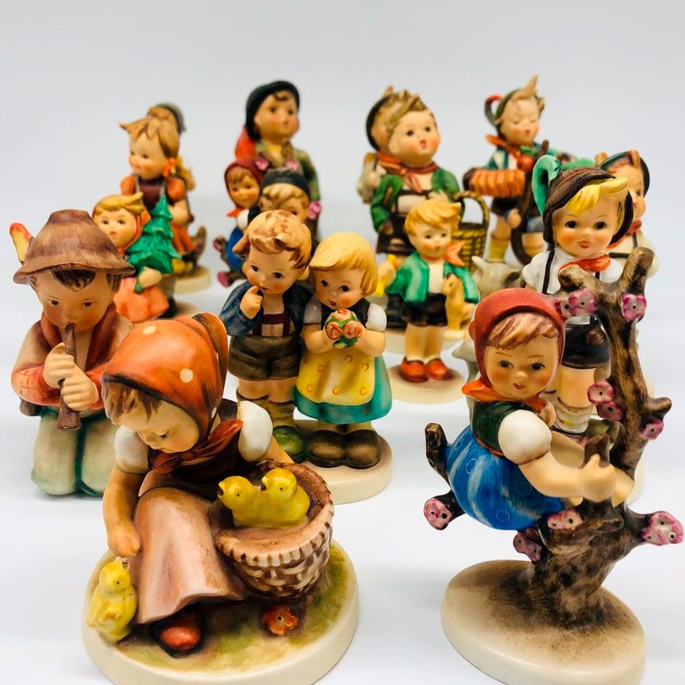 A group of colorful ceramic figurines depicting children in traditional clothing, engaged in various activities such as playing, climbing a tree, and tending to animals, are displayed closely together against a plain background.