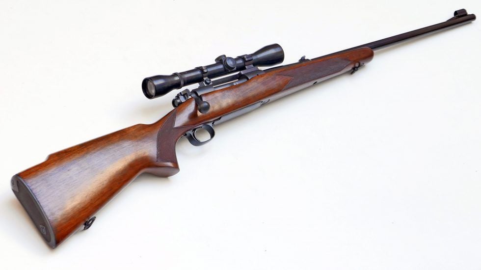 A bolt-action hunting rifle with a wooden stock and a mounted scope, displayed on a plain white background.