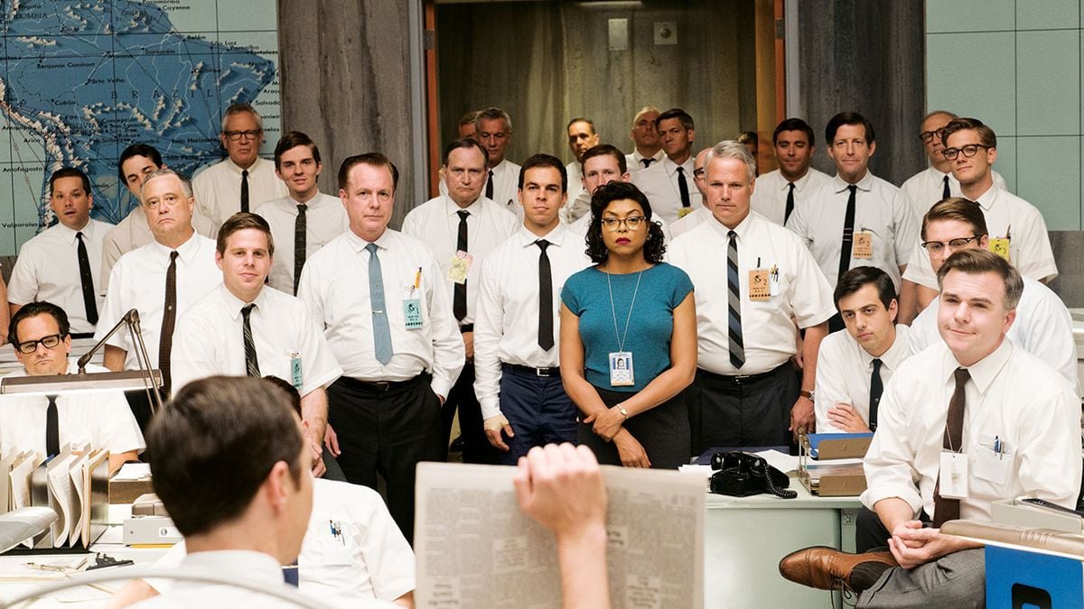 A group of men in white shirts and ties stand around a woman in a blue dress at a busy vintage office, appearing focused on someone reading a newspaper in the foreground. A large world map is visible on the wall.