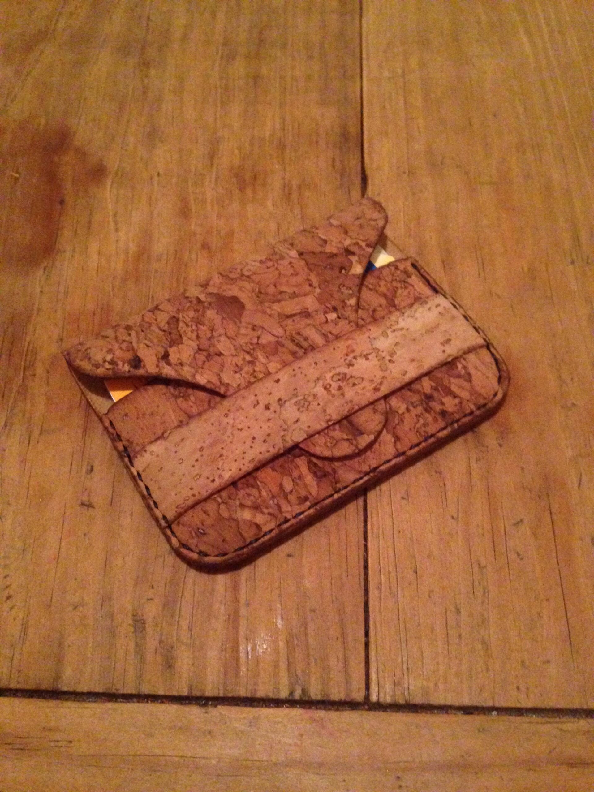 A cork wallet with a front flap and visible cards inside, lying on a wooden surface.