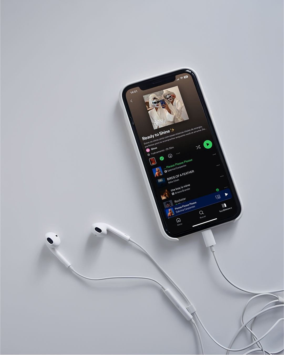 A smartphone with white wired earphones displays a Spotify playlist titled "Ready to Shine" on its screen, set against a plain light grey background.