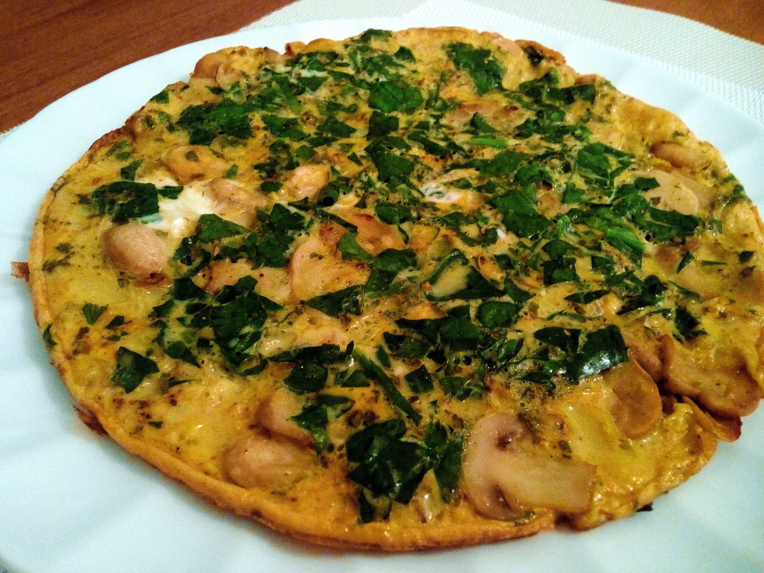 A cooked omelette with chopped spinach and sliced mushrooms on a white plate, placed on a table with a textured tablecloth.