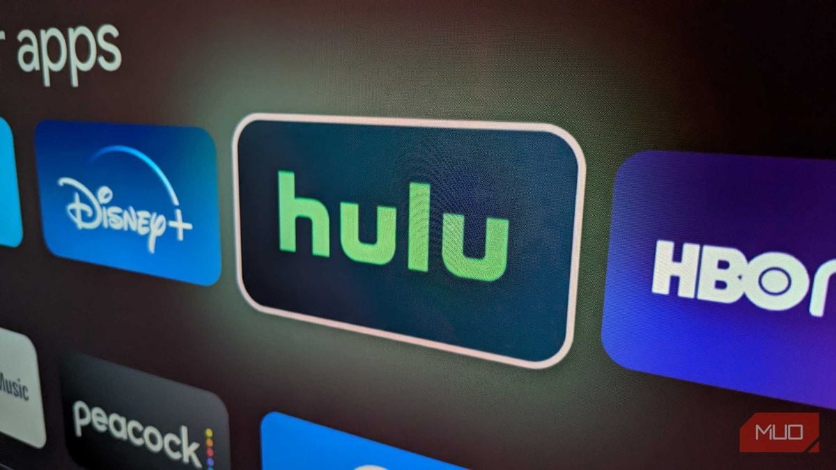 A close-up of a TV screen displaying streaming app icons, including Hulu, Disney+, HBO, and Peacock. The Hulu icon is highlighted in the center.