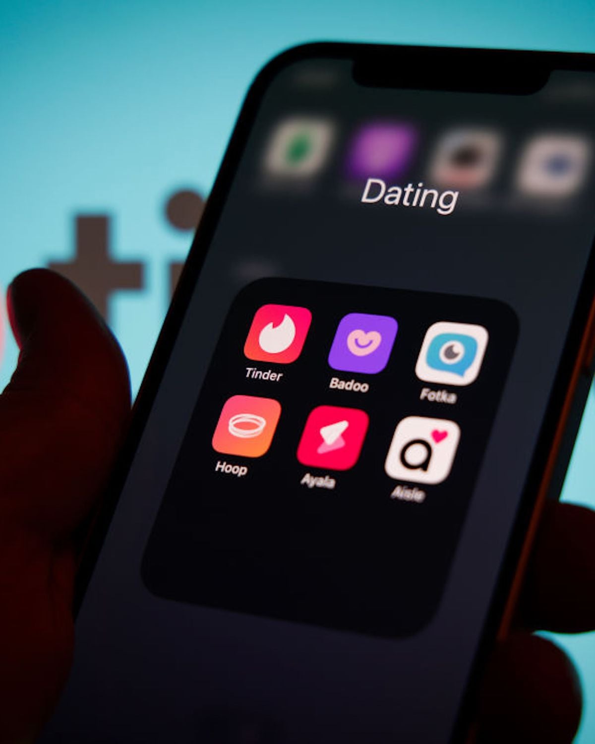 A smartphone screen displays a folder labeled "Dating" containing six app icons: Tinder, Badoo, Fotka, Hoop, Aya, and Aisle, with a blurred background.