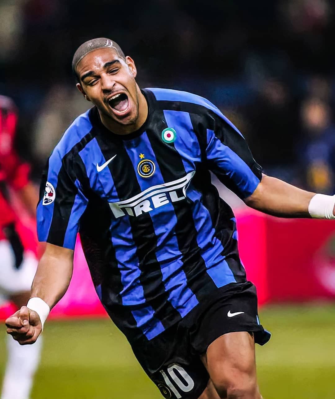 A soccer player in a blue and black striped Inter Milan jersey celebrates with his mouth open and arms outstretched during a match.
