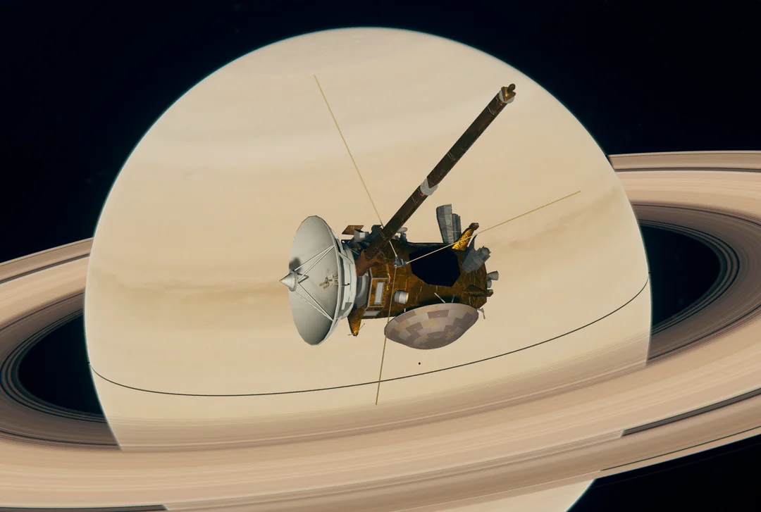 A spacecraft with a large dish antenna and extended instruments orbits close to Saturn, with the planet’s rings and pale yellow atmosphere prominently visible in the background.