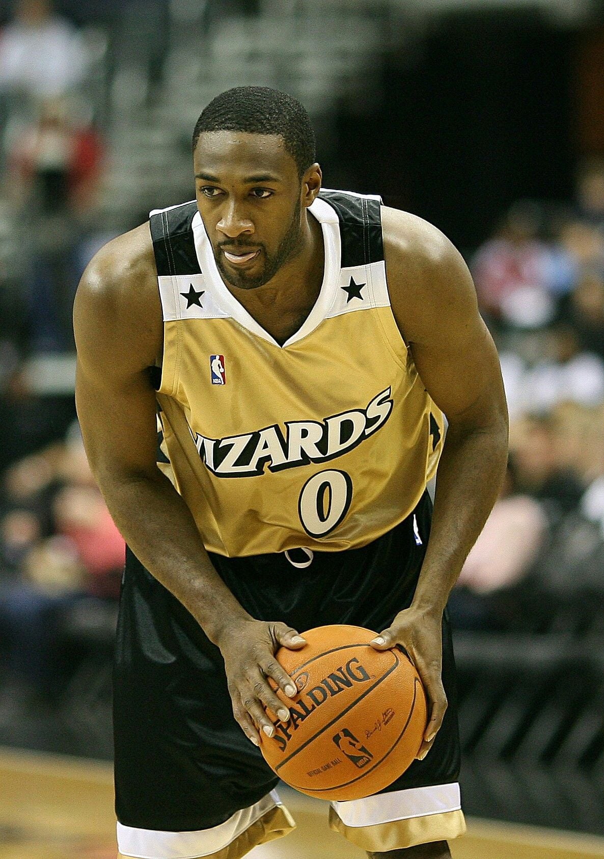 A basketball player in a gold and black Wizards jersey, number 0, prepares to take a free throw while holding a Spalding basketball on a court.