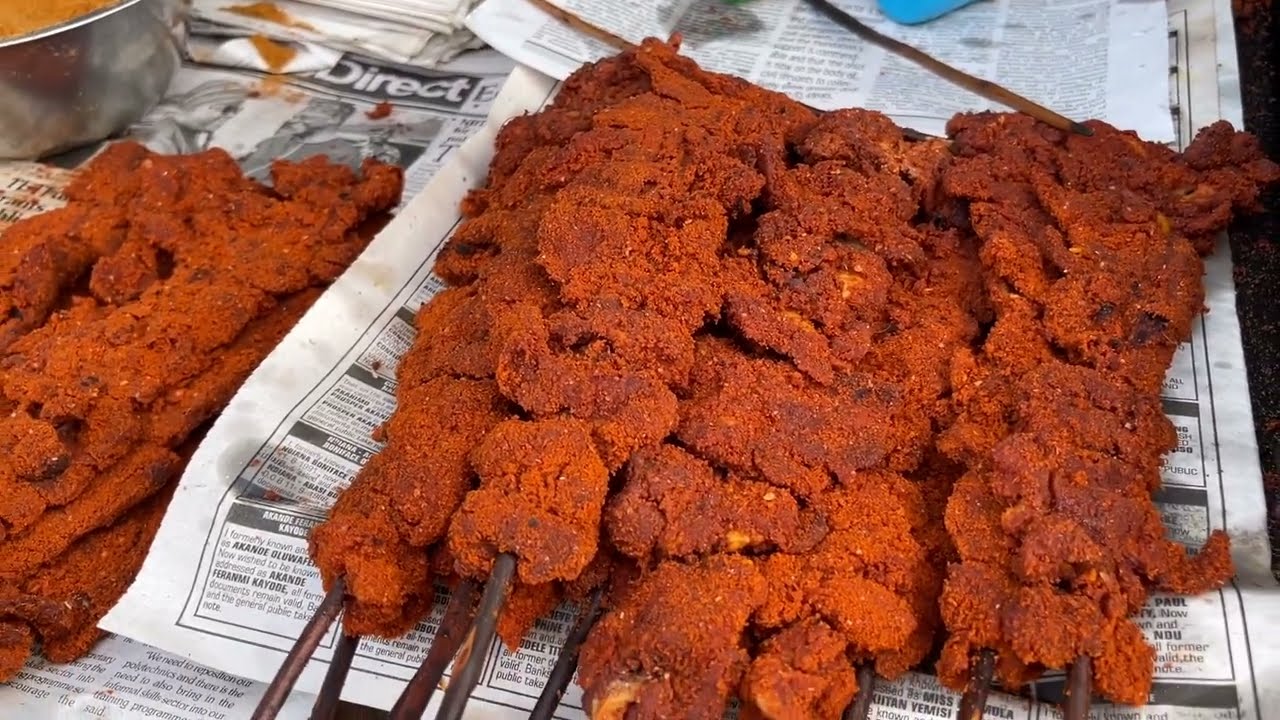 Several skewers of spicy, deep-fried meat coated in a red, crispy batter are arranged on sheets of newspaper at a street food stall.