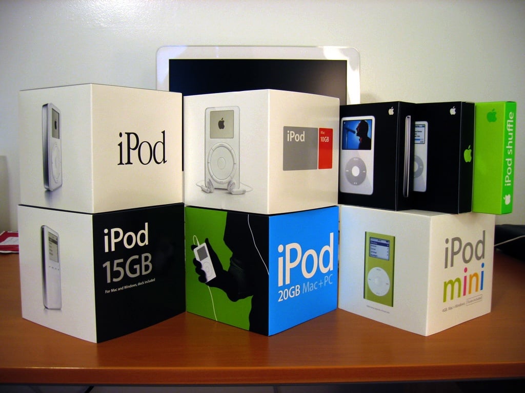 Several different iPod boxes, including iPod mini, iPod shuffle, and various classic iPod models, are displayed on a wooden desk in front of a computer monitor.
