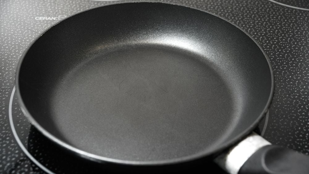 A black nonstick frying pan with a metal handle sits on a black electric stovetop with visible burner rings.