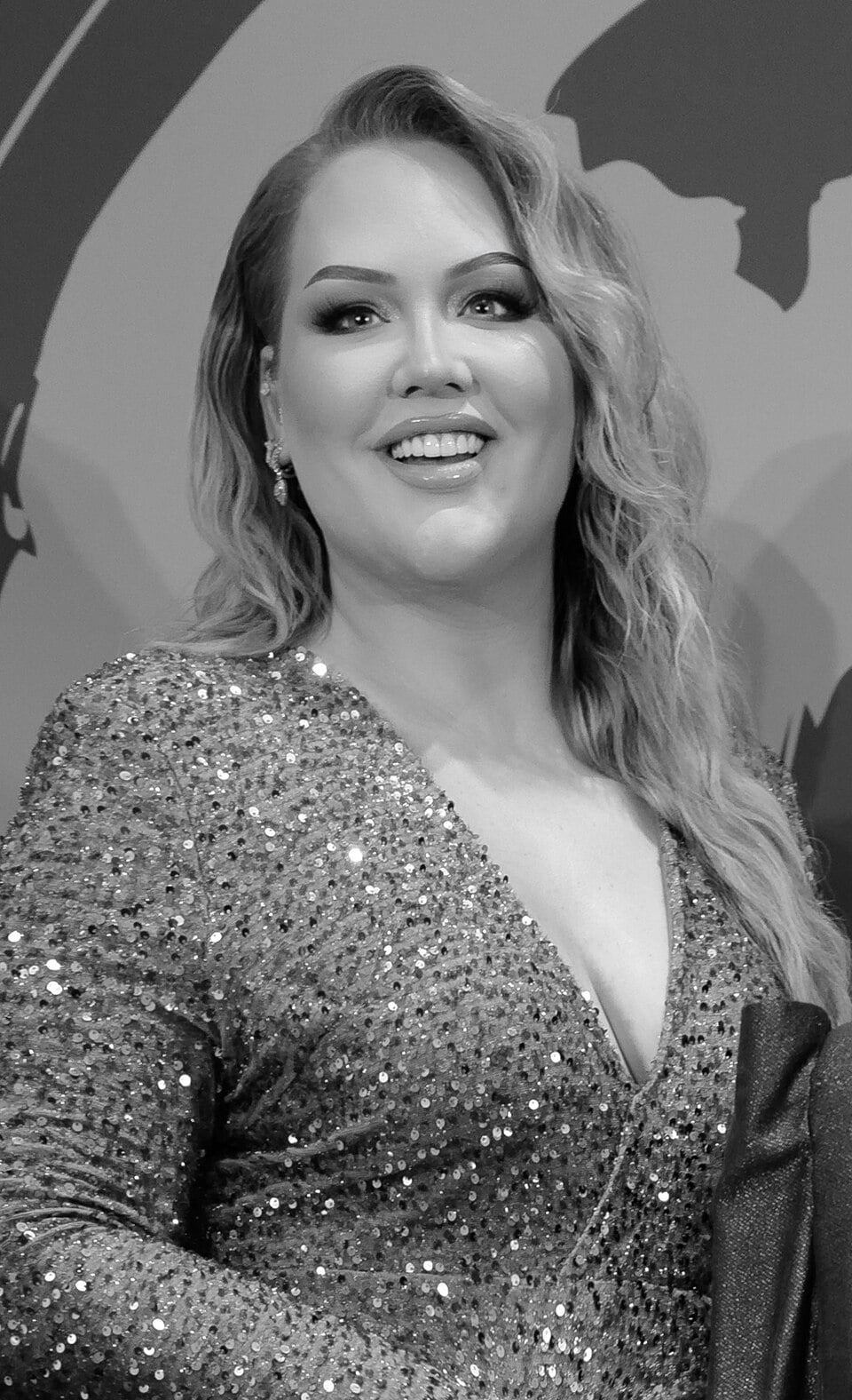 A woman with long wavy hair, wearing a sparkling sequined dress, smiles while looking slightly to the side. The image is in black and white and has a patterned background.