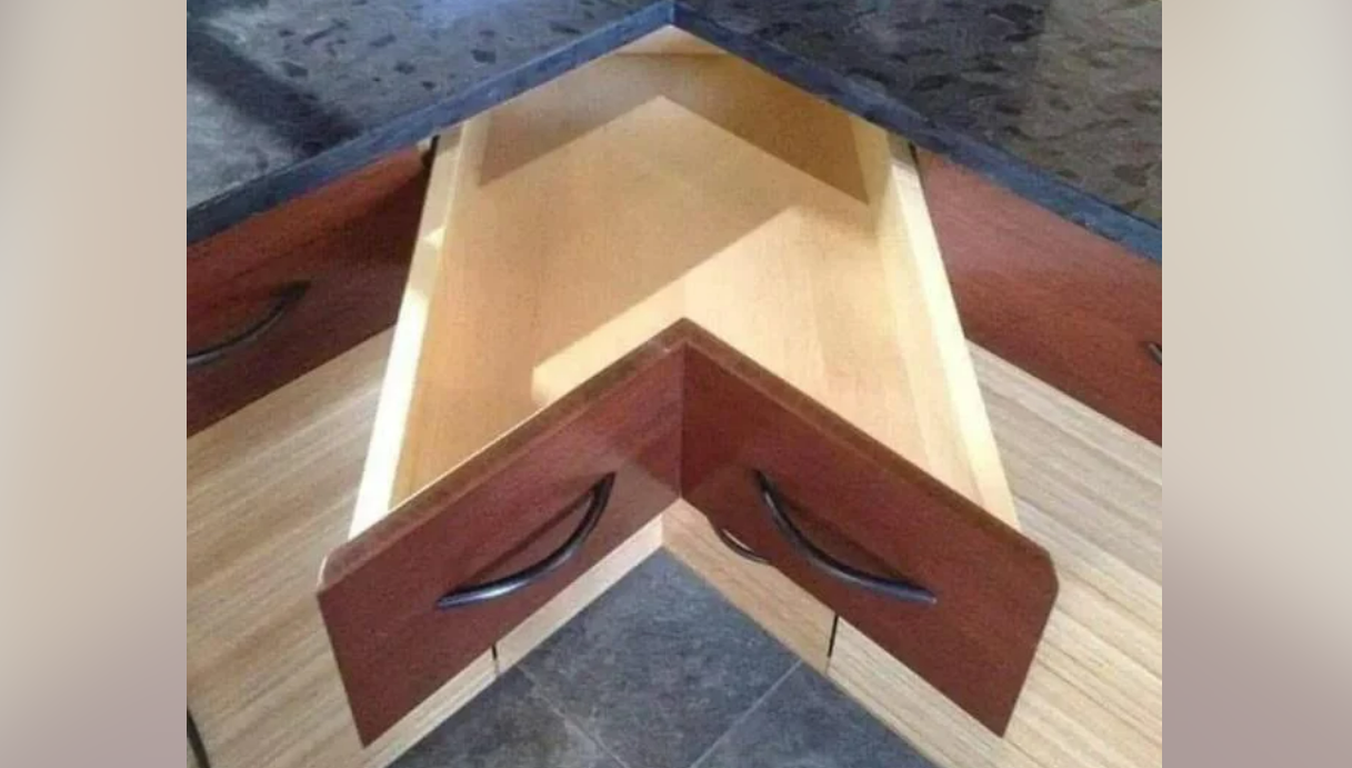 A corner kitchen drawer is open, designed in a V-shape to fit into the corner of the countertop, showing an unusual and creative storage solution.