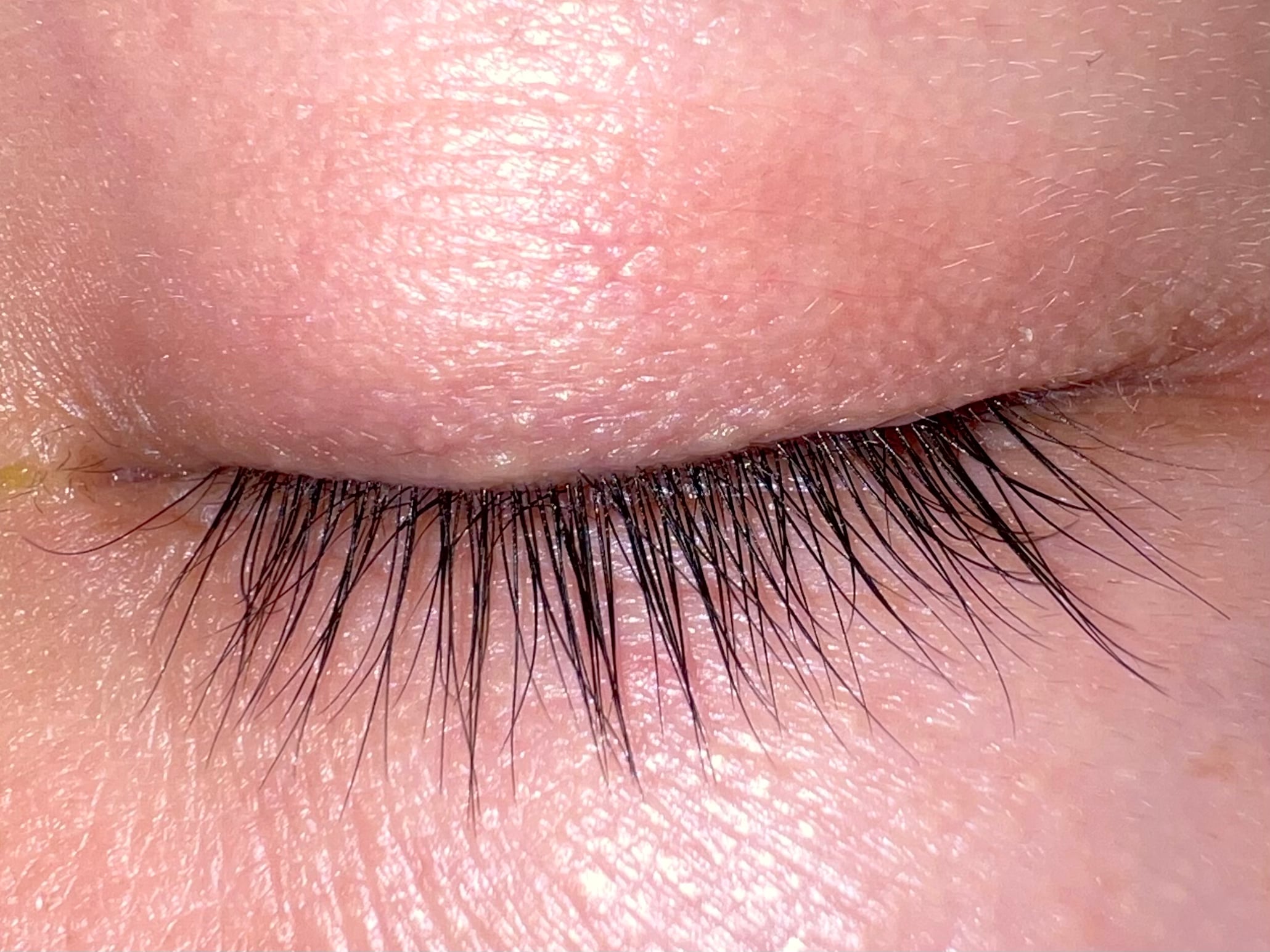 Close-up of a person's closed eye showing long, dark eyelashes and detailed skin texture on the eyelid and surrounding area.