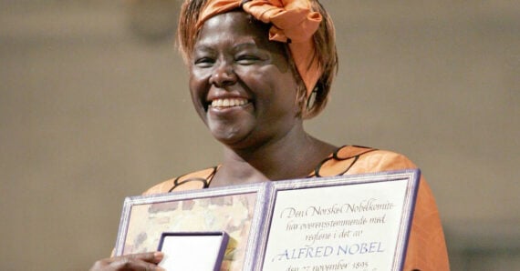 A smiling woman in an orange headscarf and dress holds up a framed Nobel Prize certificate.