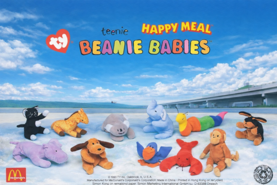 A group of colorful Teenie Beanie Babies plush toys are arranged on a light surface outdoors, with a blue sky and a bridge in the background. The image features McDonald&rsquo;s and Ty logos, promoting a Happy Meal.
