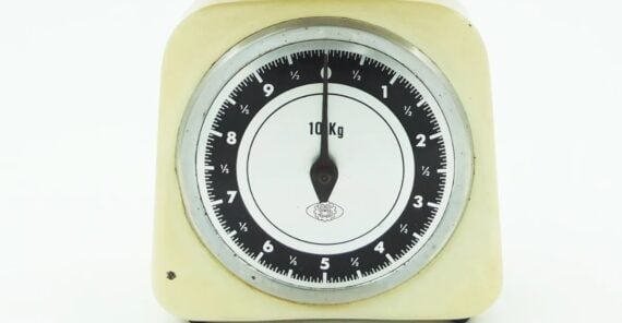 A close-up of a vintage analog kitchen scale with a cream-colored frame, displaying a measurement of 0 kg on its black and white dial, which has a maximum capacity of 10 kg.