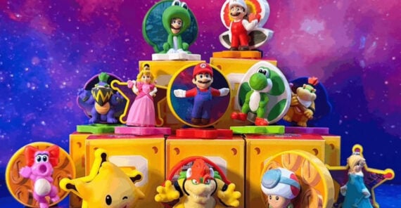 A group of colorful Super Mario character toys, including Mario, Princess Peach, Yoshi, Bowser, Toad, and others, arranged in a pyramid on yellow question mark blocks, with a vibrant purple and pink galaxy background.