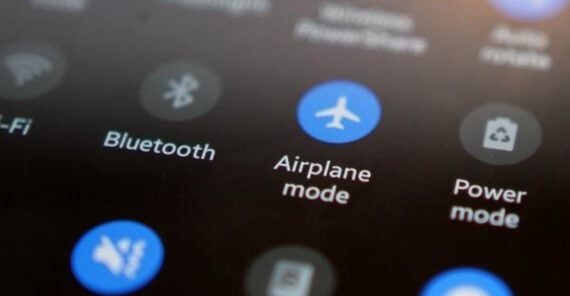 A close-up of a smartphone screen displaying quick settings icons, including Wi-Fi, Bluetooth, Airplane mode, and Power mode, with Airplane mode highlighted in blue.